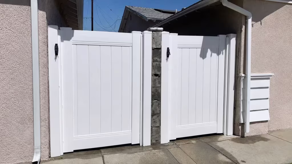 White vinyl privacy gate panels sit close to the concrete driveway with gutters visible along the roofline in Carson