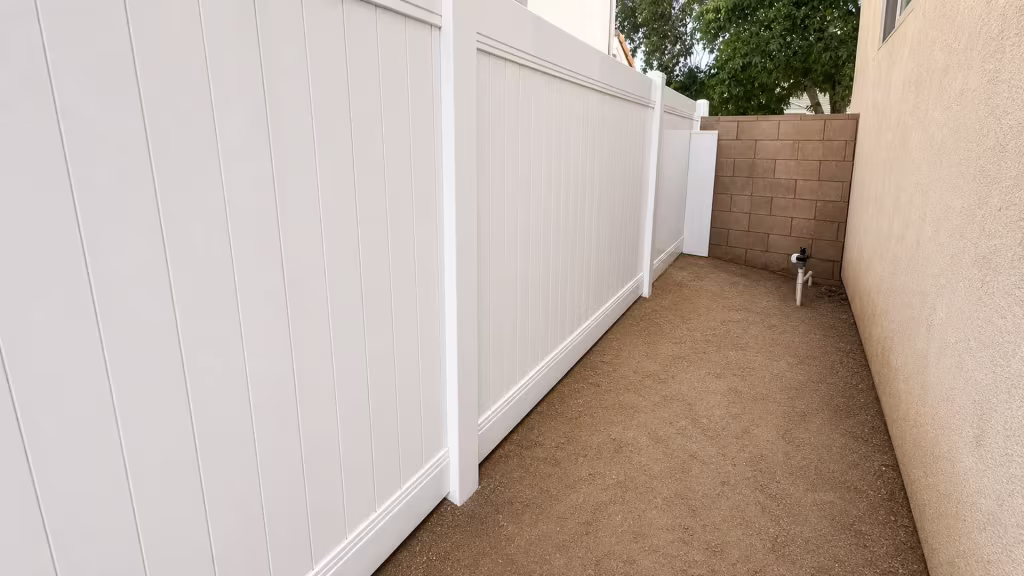 Utility pipes and a meter line the rear wall behind this White vinyl privacy fence in Palmdale