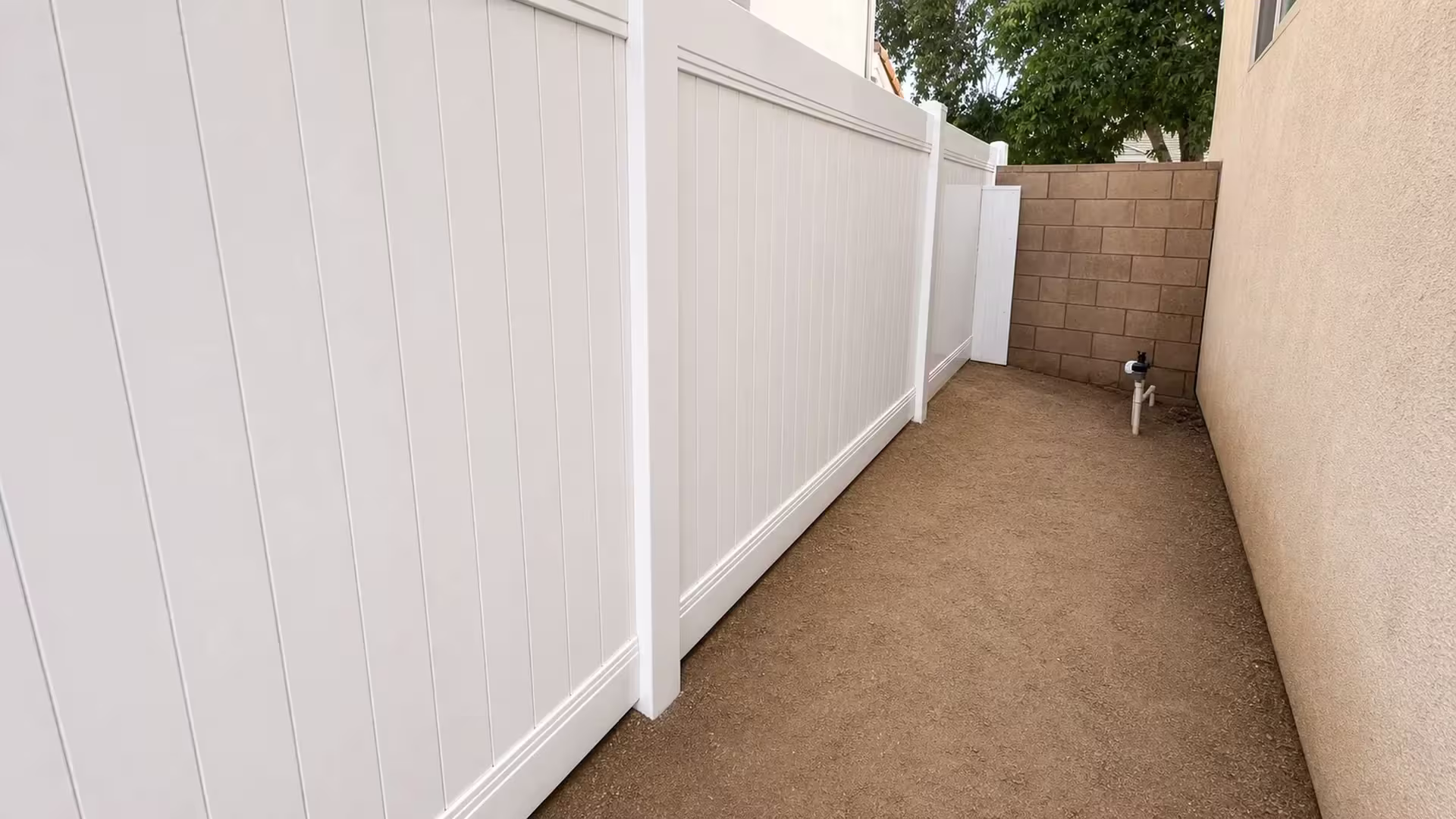 Utility pipes and a meter line the rear wall behind this White vinyl privacy fence in Palmdale