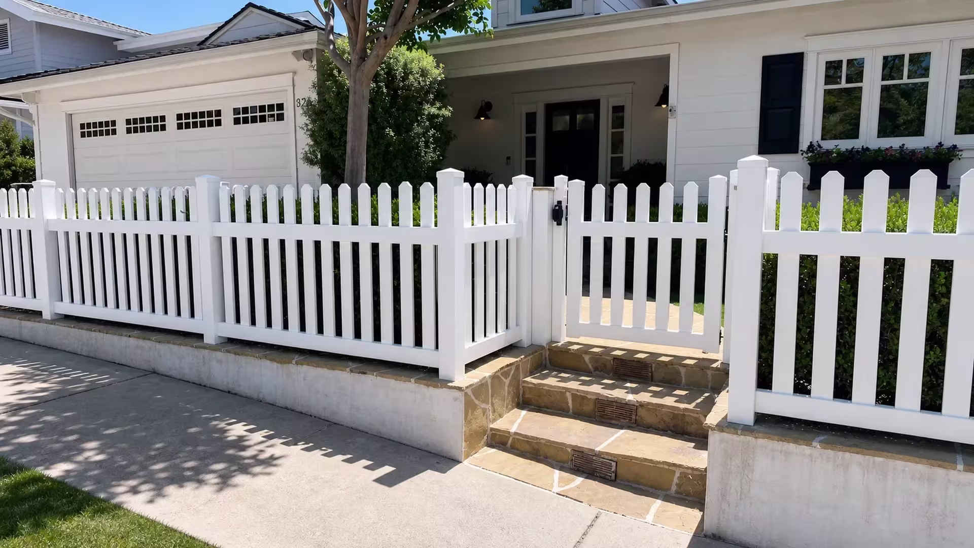 A pedestrian gate opens through the White vertical vinyl picket fence beside a mature tree at this Pacific Palisades entry