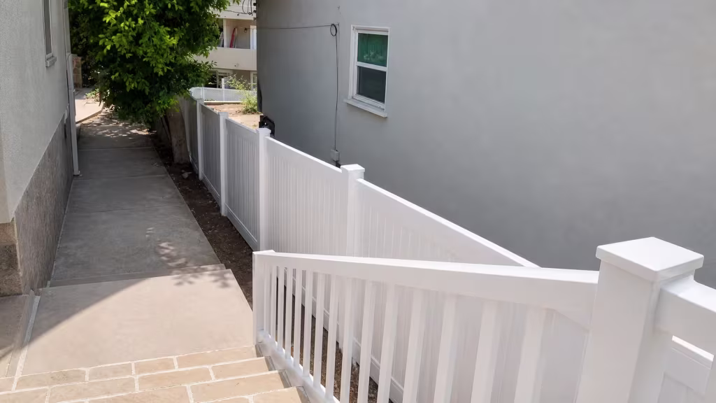 Tiled stairs descend beside a sloped White vertical vinyl picket fence at this Pacific Palisades house