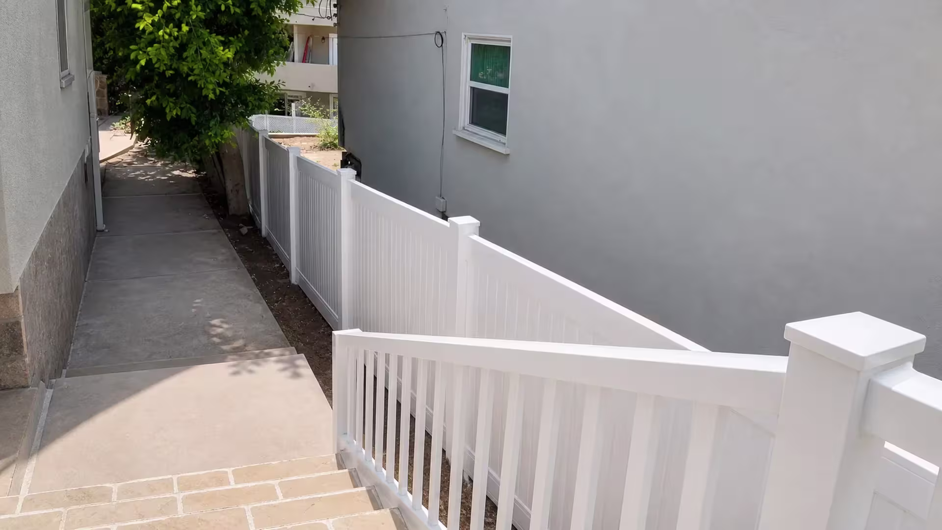 Tiled stairs descend beside a sloped White vertical vinyl picket fence at this Pacific Palisades house