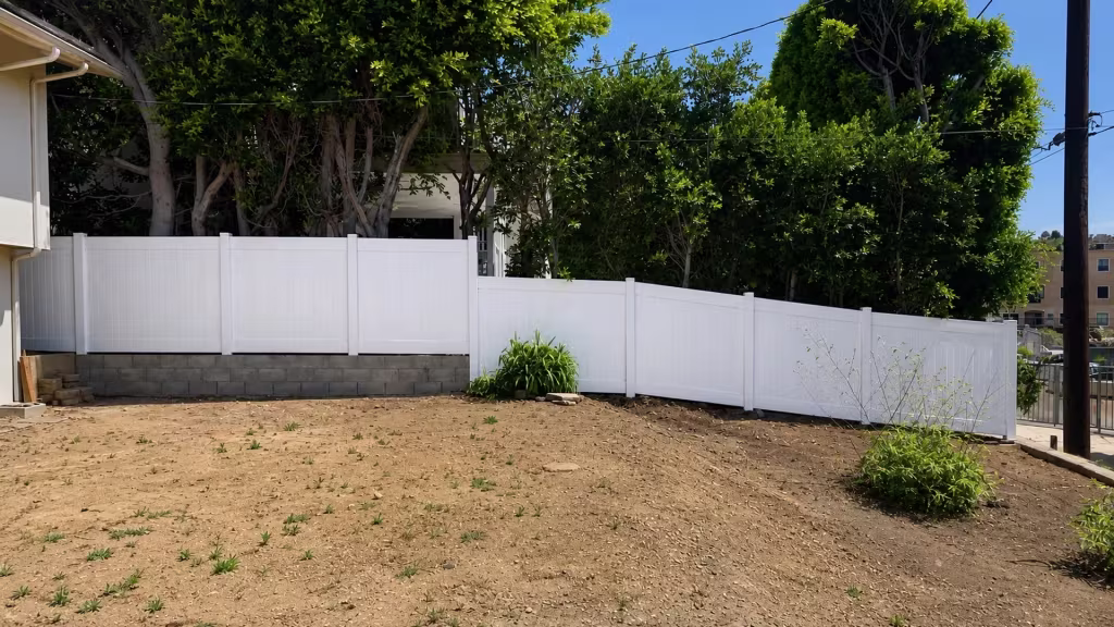 A wooden utility pole rises beside the White vertical vinyl picket fence descending this Pacific Palisades backyard