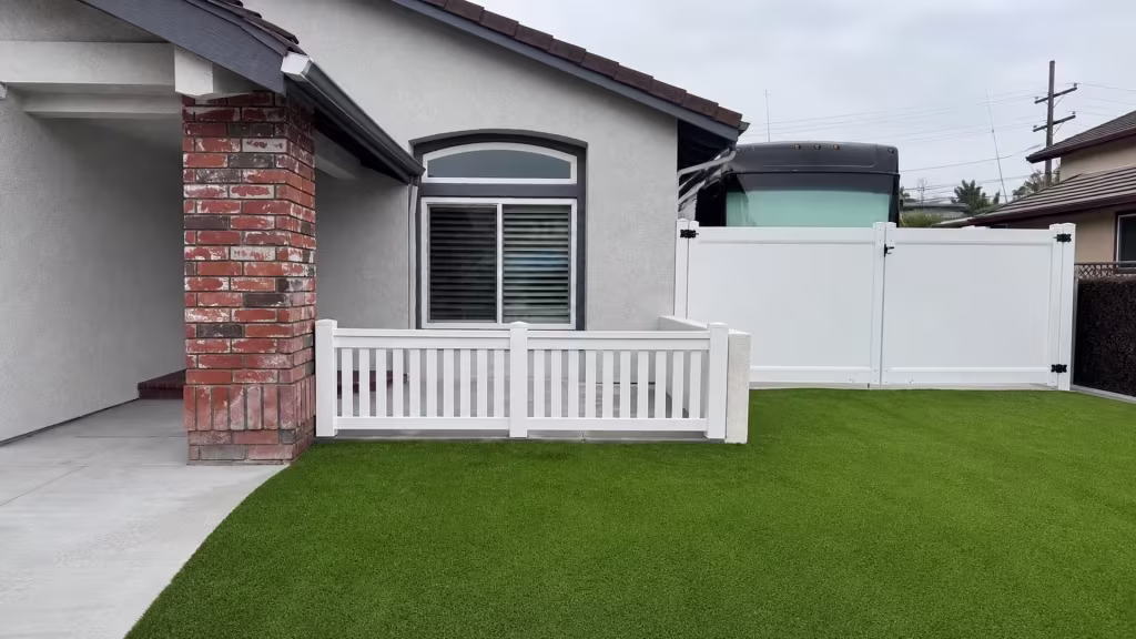A White picket fence, built in vinyl, runs low along the Yorba Linda walkway, with utility poles and rooflines beyond