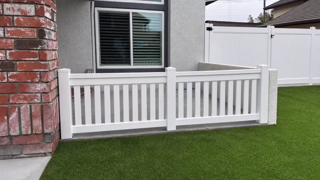 A White vertical vinyl picket fence rises from artificial turf beneath an arched window transom in Yorba Linda