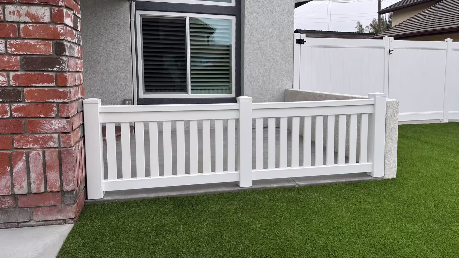 A White vertical vinyl picket fence rises from artificial turf beneath an arched window transom in Yorba Linda