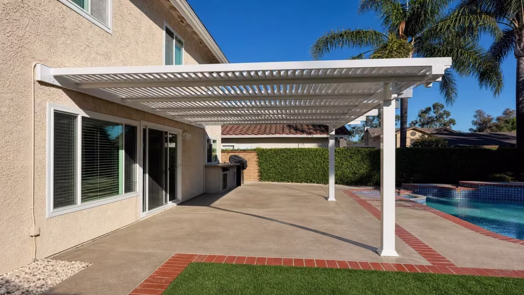 Neighboring rooflines and brickwork rise past the pool coping beside this White vinyl pergola cover in Thousand Oaks