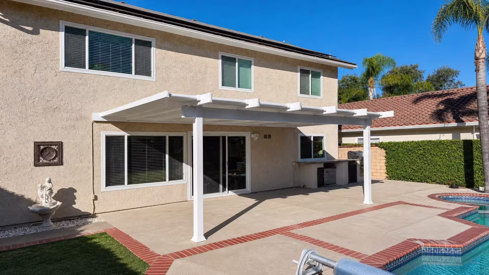White vinyl pergola cover with slatted rafters spanning the rear wall of a two-story stucco house