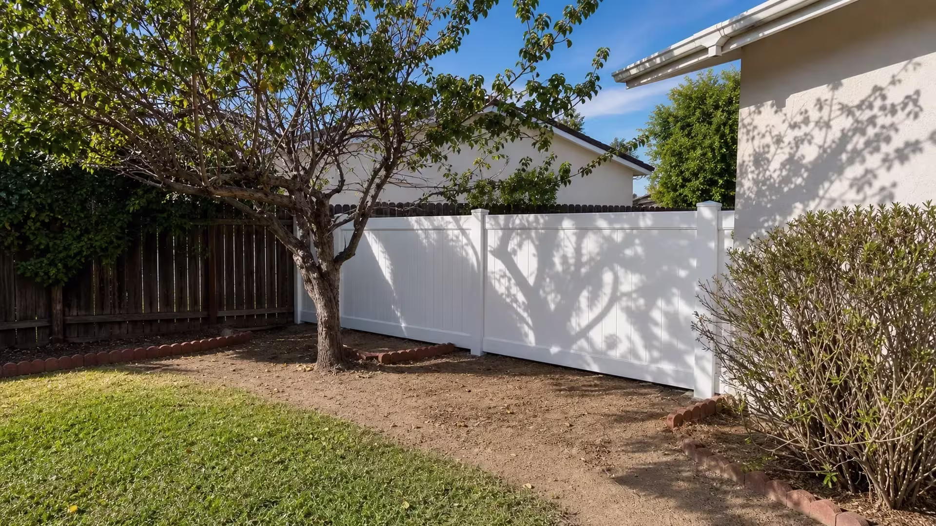 In Arcadia, an older dark wood boundary fence stands behind this White vinyl privacy fence