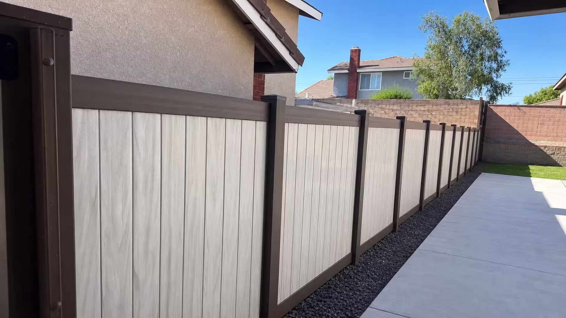 Dark Walnut and aspen two-tone vinyl privacy fence running past a gravel bed in Chino