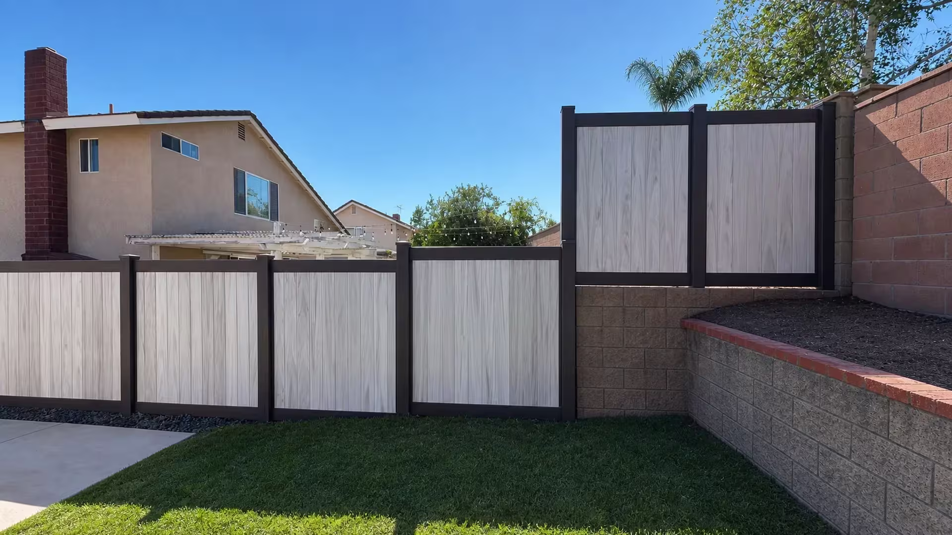 Two-tone vinyl privacy fence pairs Dark Walnut framing with pale Aspen boards on a terraced retaining wall in Chino