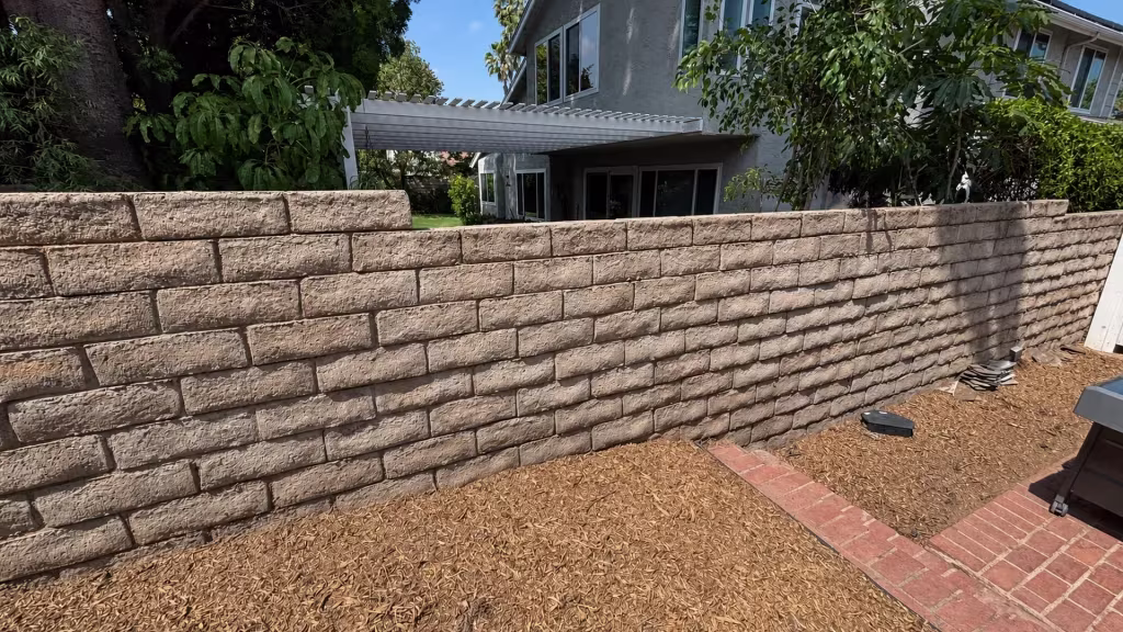 Before installation, a bare block wall separates the yard from a neighboring patio and white pergola.