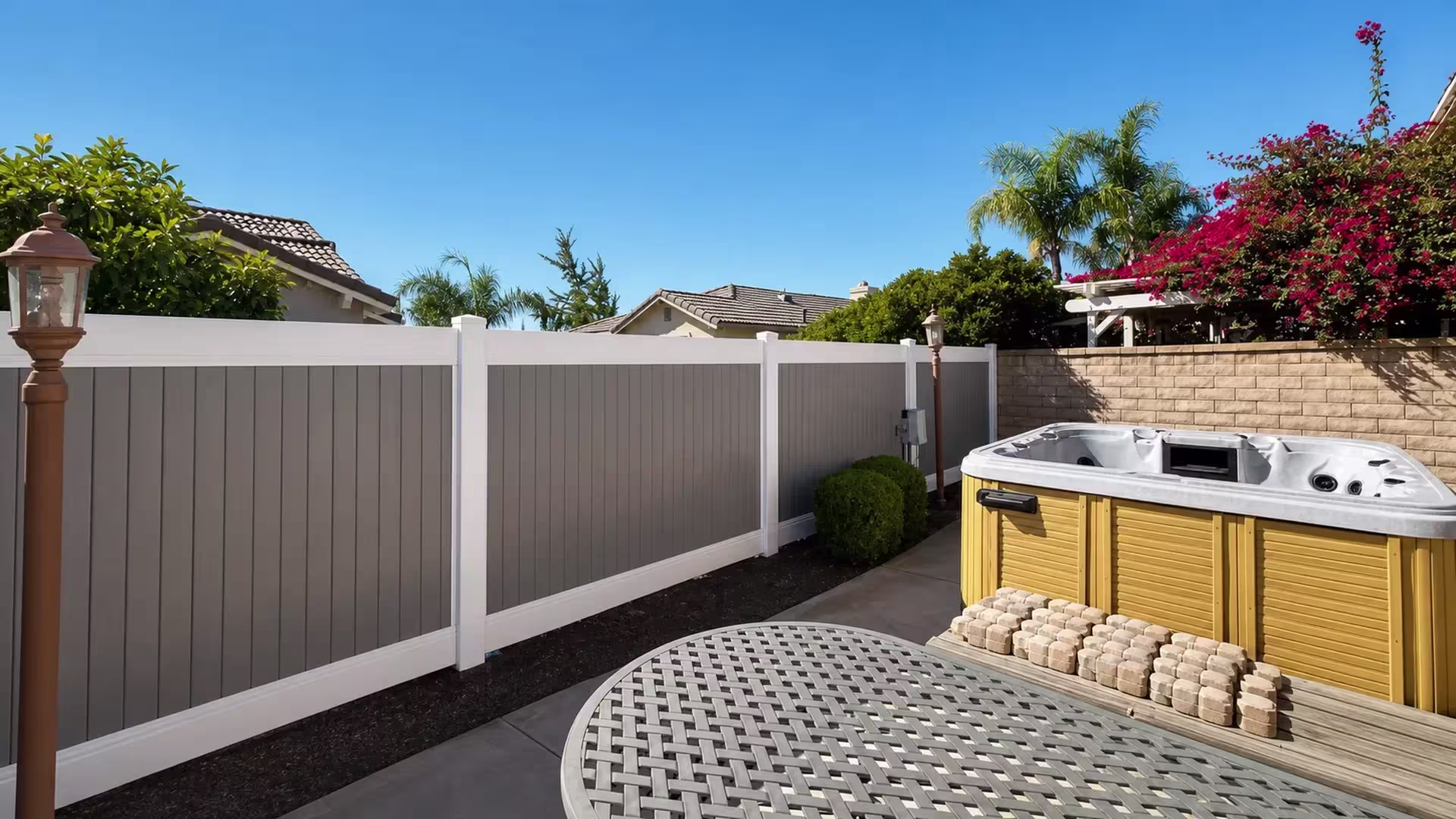 Gray vinyl boards form this two-tone privacy fence tracing the patio's concrete edge near the hot tub in Rancho Cucamonga