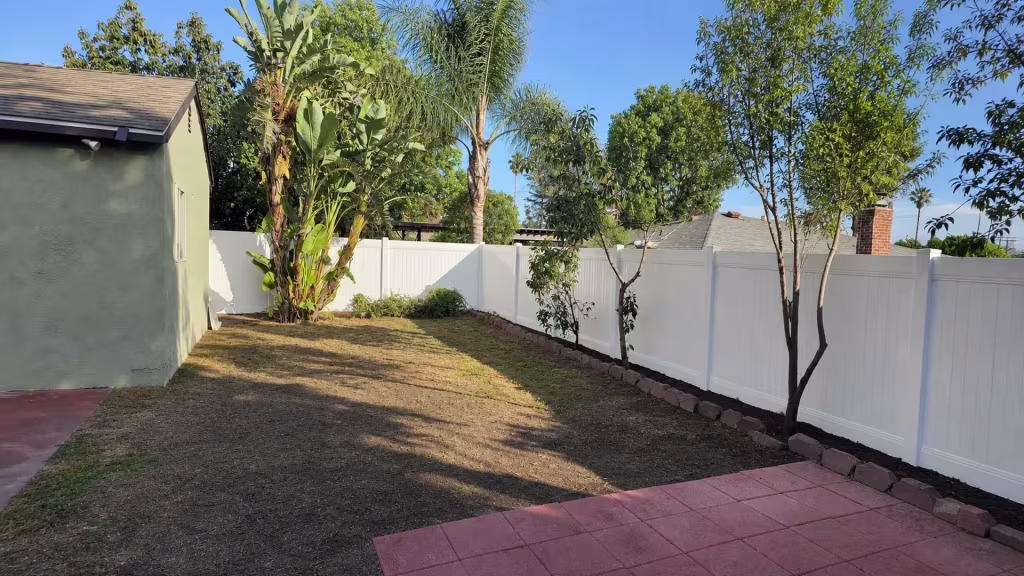 A pink-tan stone border and planting strip run beside this White vinyl fence wrapping a Pasadena backyard