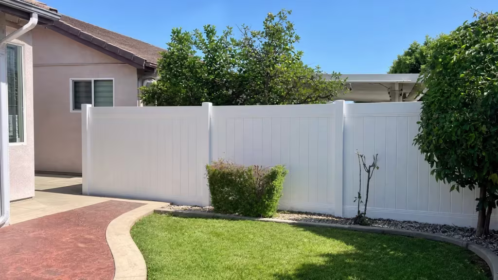 Sparse rose stems and a curved lawn edge run beside this White vinyl fence lining a stamped concrete walk in Duarte