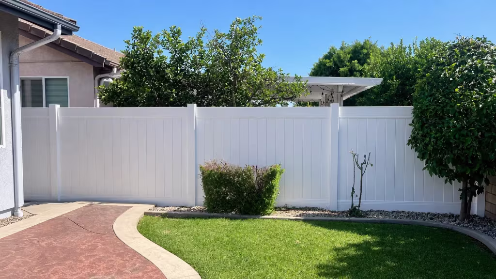 A red-and-tan walkway curves beside the lawn edge where White vinyl fence boards run through this Duarte yard