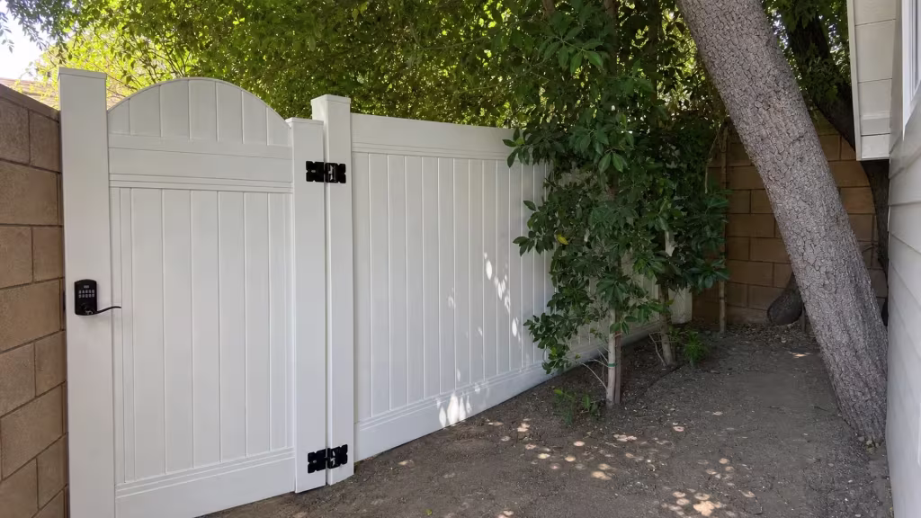 A black keypad latch secures the arched gate on this vinyl fence, finished in White, in a shaded San Marino side yard