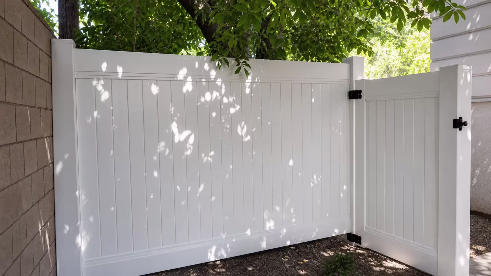 A tan masonry wall and the house itself flank the gate and privacy fence panels of this White vinyl run in San Marino