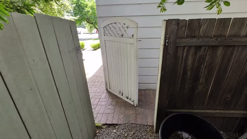 Before installation, several mismatched old wood gates open onto a brick walkway beside the house.