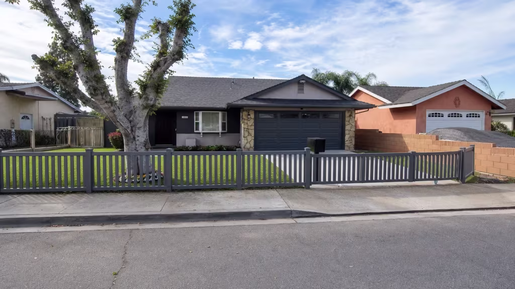 Vinyl picket fence in Arctic Blend spans the Whittier driveway edge toward a tan block boundary wall