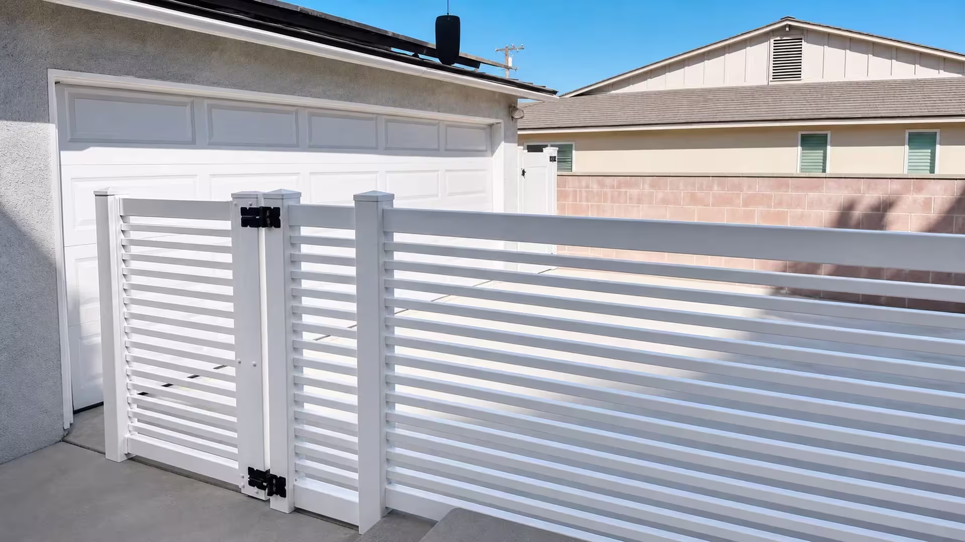 A salmon-pink concrete block wall next door borders this White vinyl horizontal picket fence through an Arcadia side yard