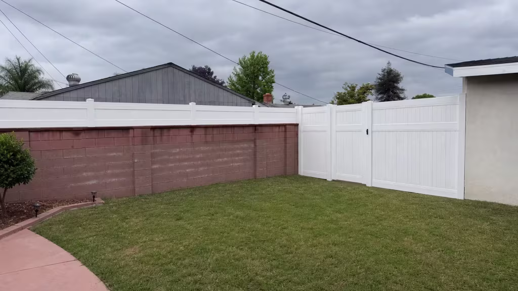 A reddish brown block wall carries this White vinyl fence at its coping line in West Covina