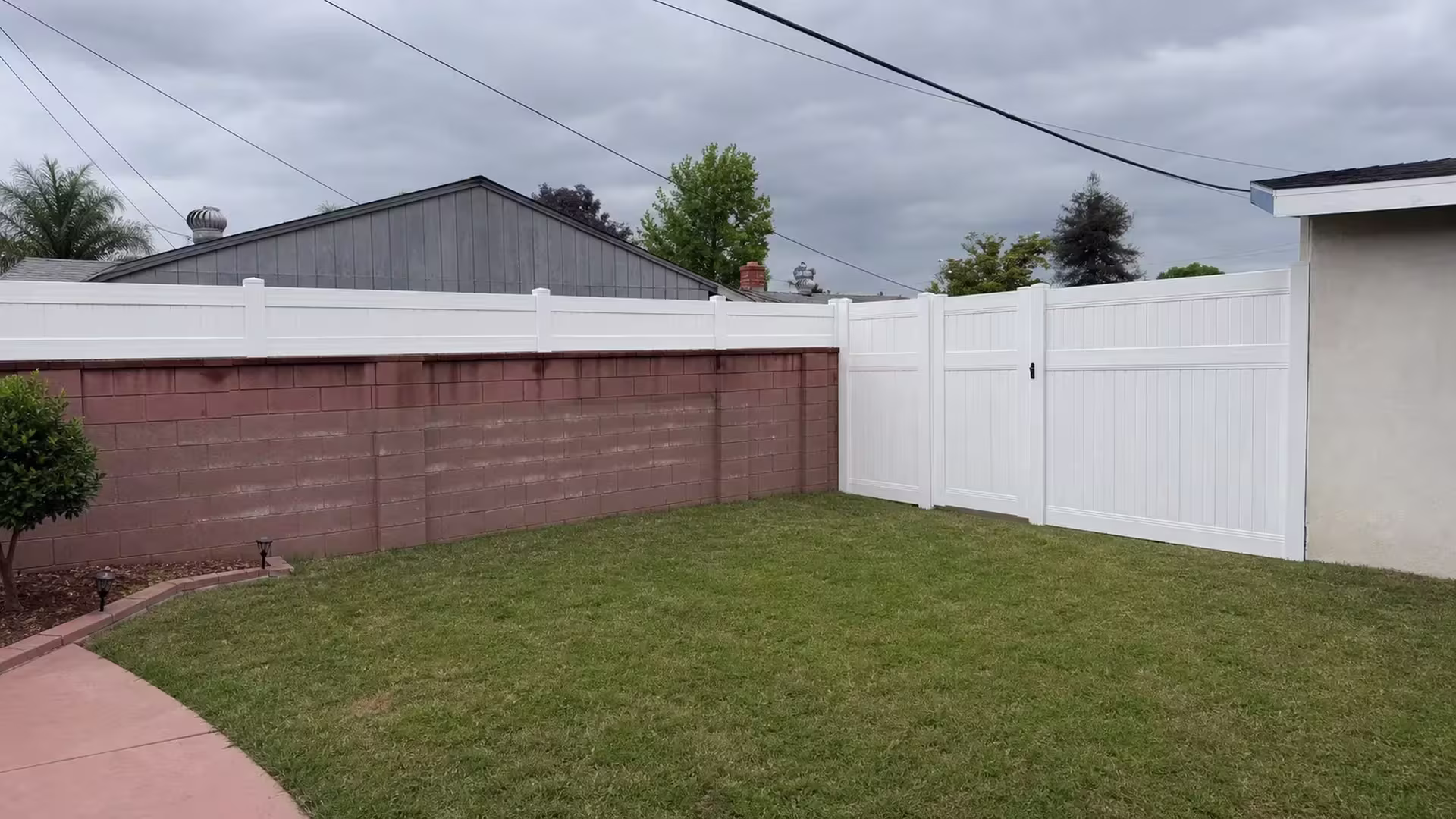A reddish brown block wall carries this White vinyl fence at its coping line in West Covina