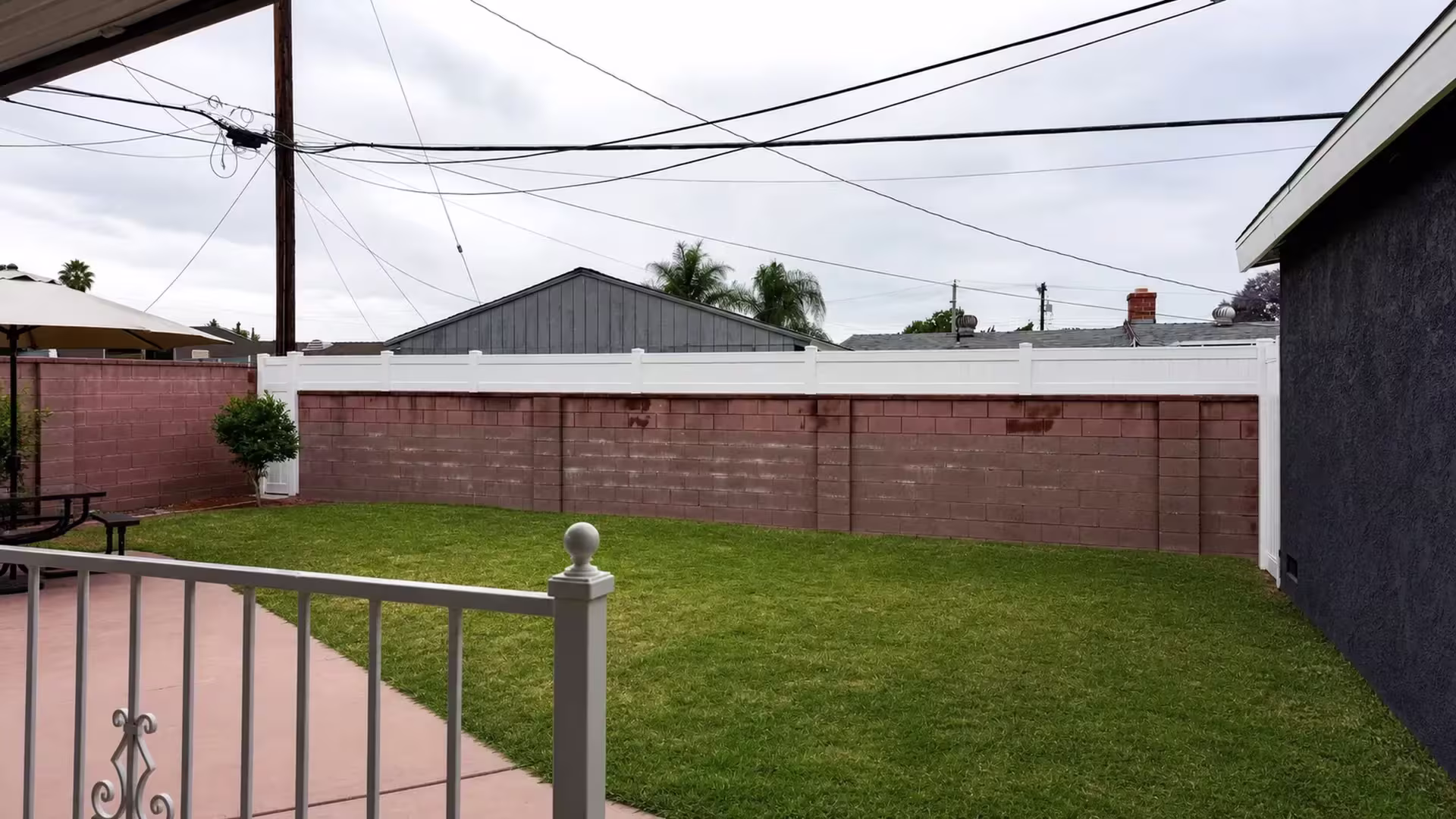 A scrolled porch railing with a round finial rises before this White vinyl privacy fence topping a wall in West Covina