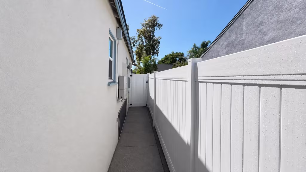 A White vinyl privacy fence and gate close the passage between a pale stucco wall and a dark boundary wall in North Hollywood