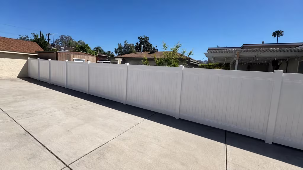A patio cover with posts and rafters stands beside this White vinyl privacy fence crossing a concrete slab in North Hollywood