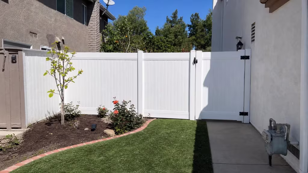 A tall masonry chimney and satellite dish stand behind this White vinyl fence and gate in Lake Forest
