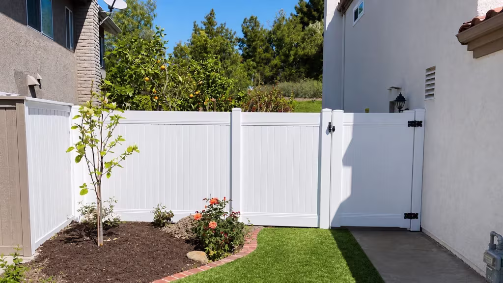 A citrus tree and satellite dish flank the gate of this White vinyl fence over an artificial-turf lawn in Lake Forest