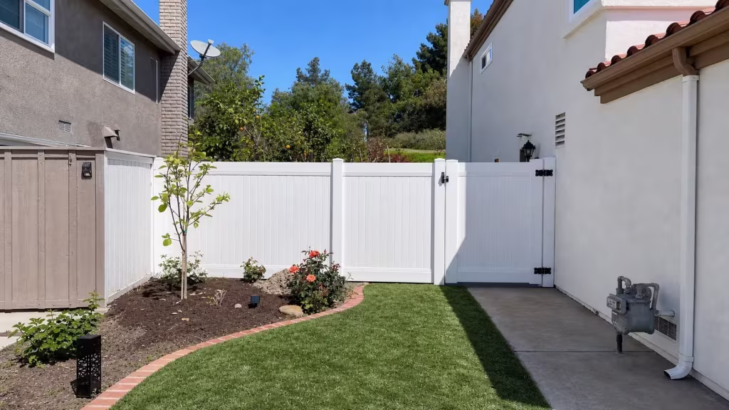 A gas meter and pipes sit beside this White vinyl privacy fence and gate spanning a narrow Lake Forest passage
