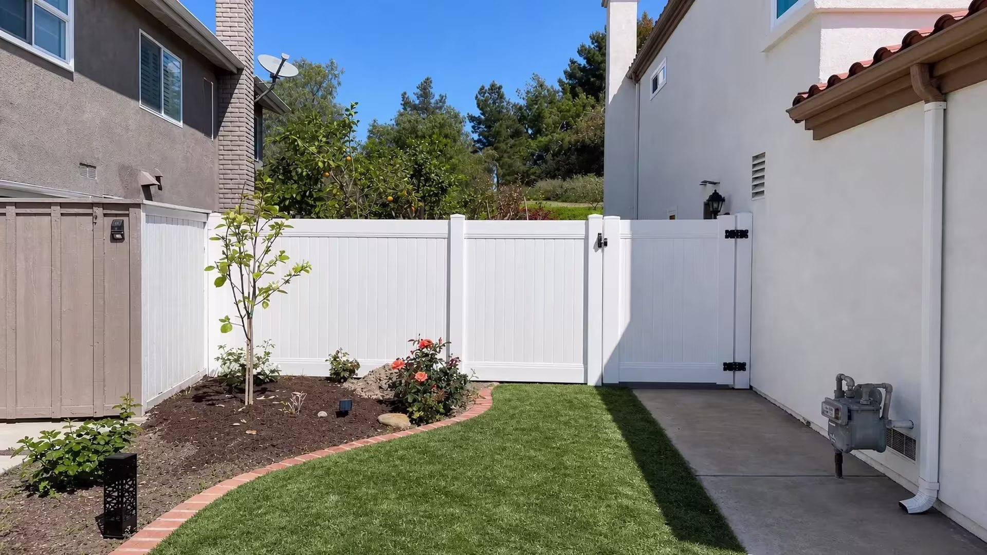 A gas meter and pipes sit beside this White vinyl privacy fence and gate spanning a narrow Lake Forest passage