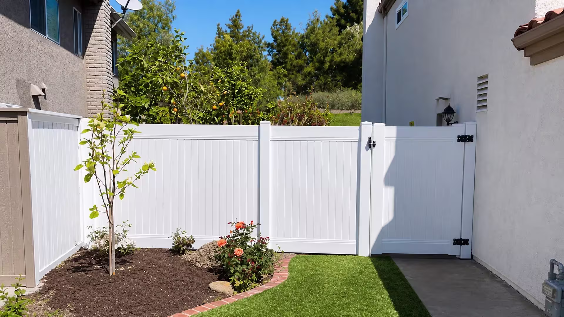 A citrus tree and satellite dish flank the gate of this White vinyl fence over an artificial-turf lawn in Lake Forest