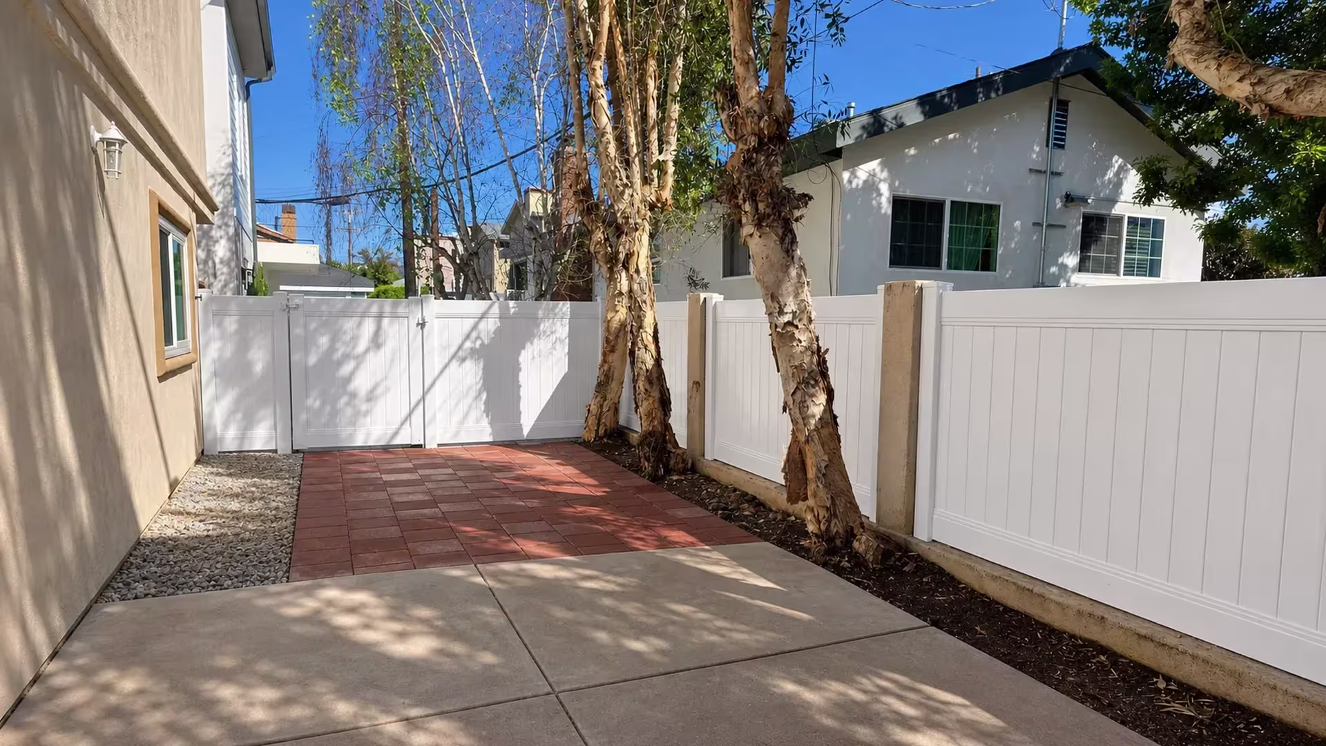 A red paver walkway leads to this White vinyl gate closing the privacy fence enclosure in Redondo Beach