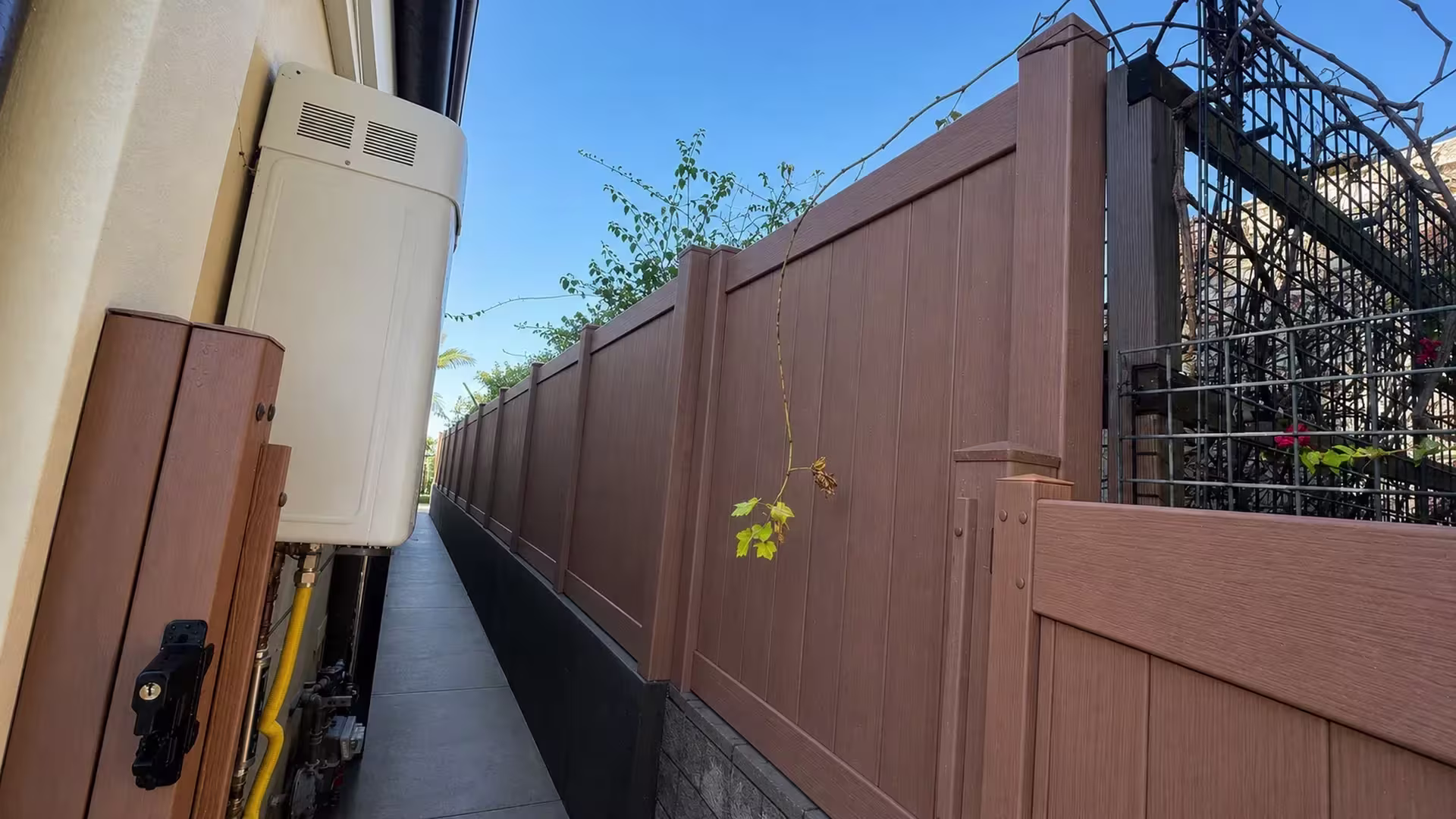 A tankless water heater and gas line sit beside this Siera Blend vinyl privacy fence along a narrow Torrance walkway