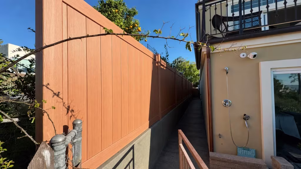 A black metal balcony railing overlooks this Siera Blend vinyl privacy fence set above a stucco retaining wall in Torrance
