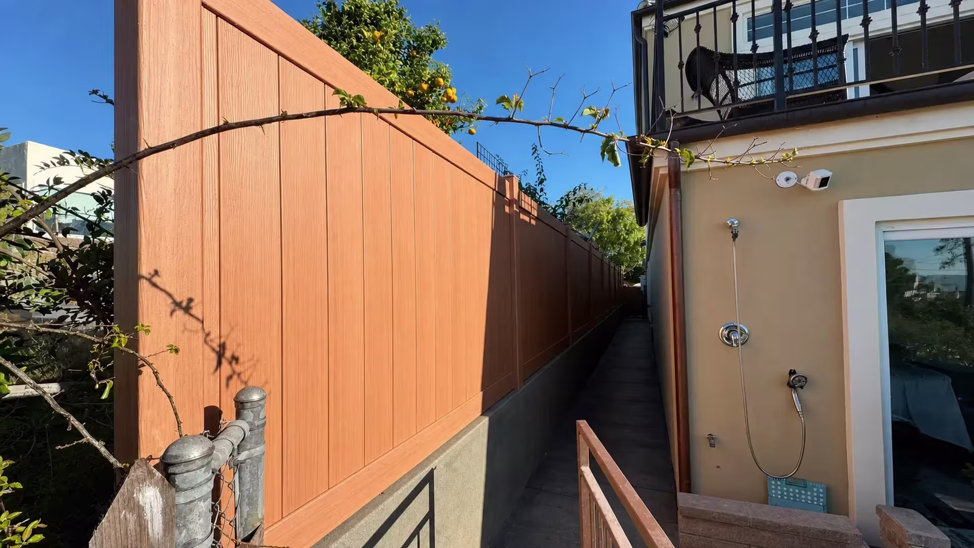 A black metal balcony railing overlooks this Siera Blend vinyl privacy fence set above a stucco retaining wall in Torrance
