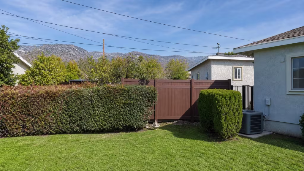 A small garden ornament sits beside this vinyl fence, finished in Dark Sequoia, with a mountain ridge behind it in Burbank