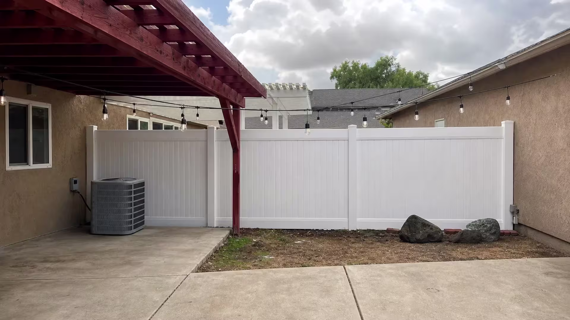 A wood pergola shades this White vinyl fence where it wraps the patio and HVAC condenser in La Verne