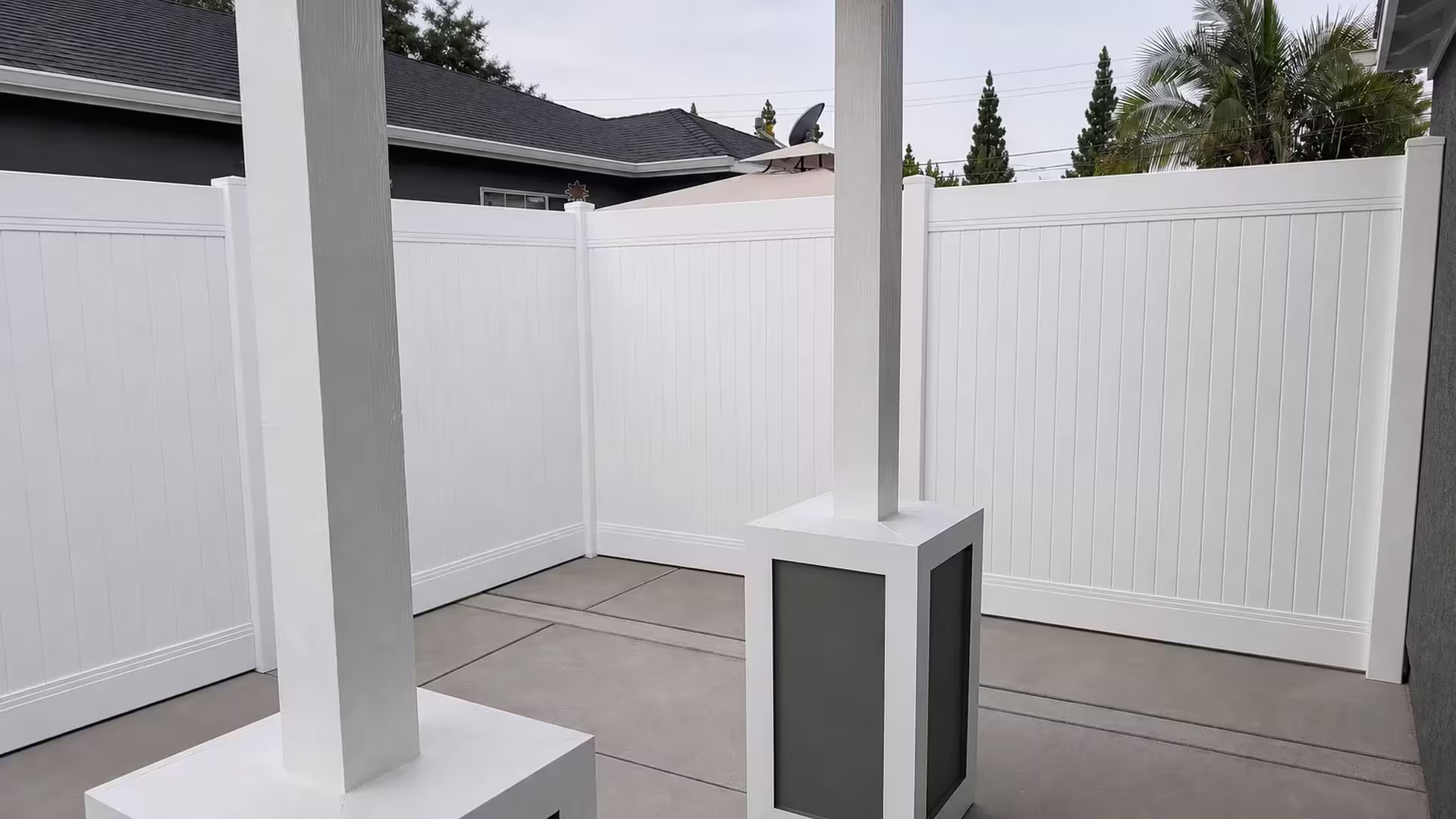 This White vinyl privacy fence turns an inside corner past a satellite dish and palm trees in Lakewood