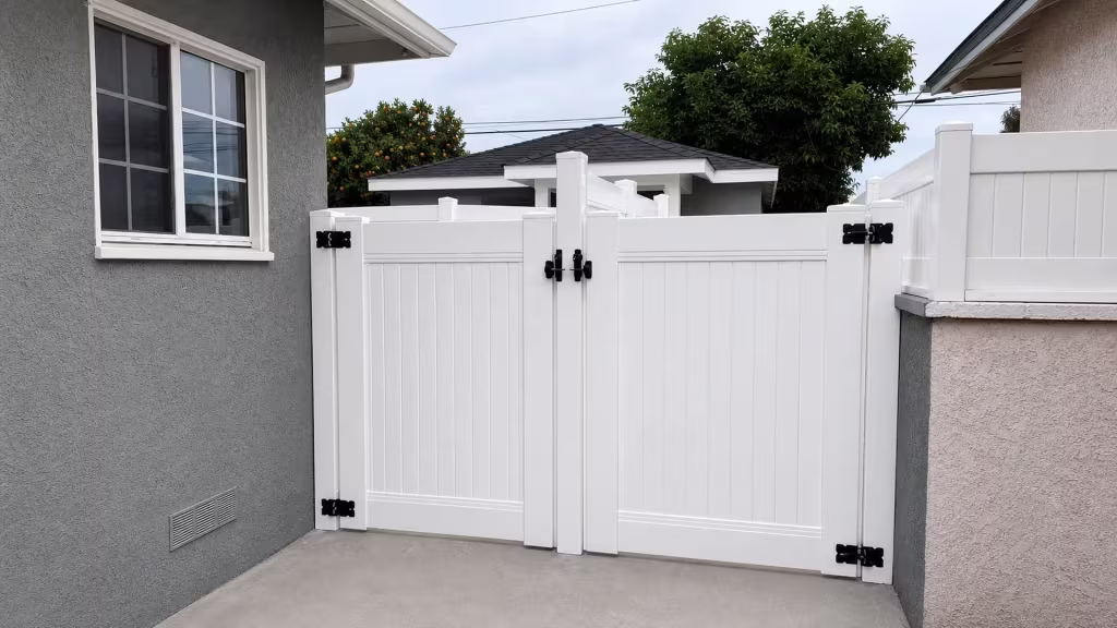 White vinyl privacy fence and gate span between a gray stucco house and a two-tone stucco wall in Lakewood