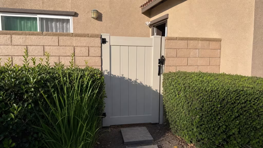 A wall lantern and curtained window sit above this closed White vinyl gate, set between tan block walls in Ontario