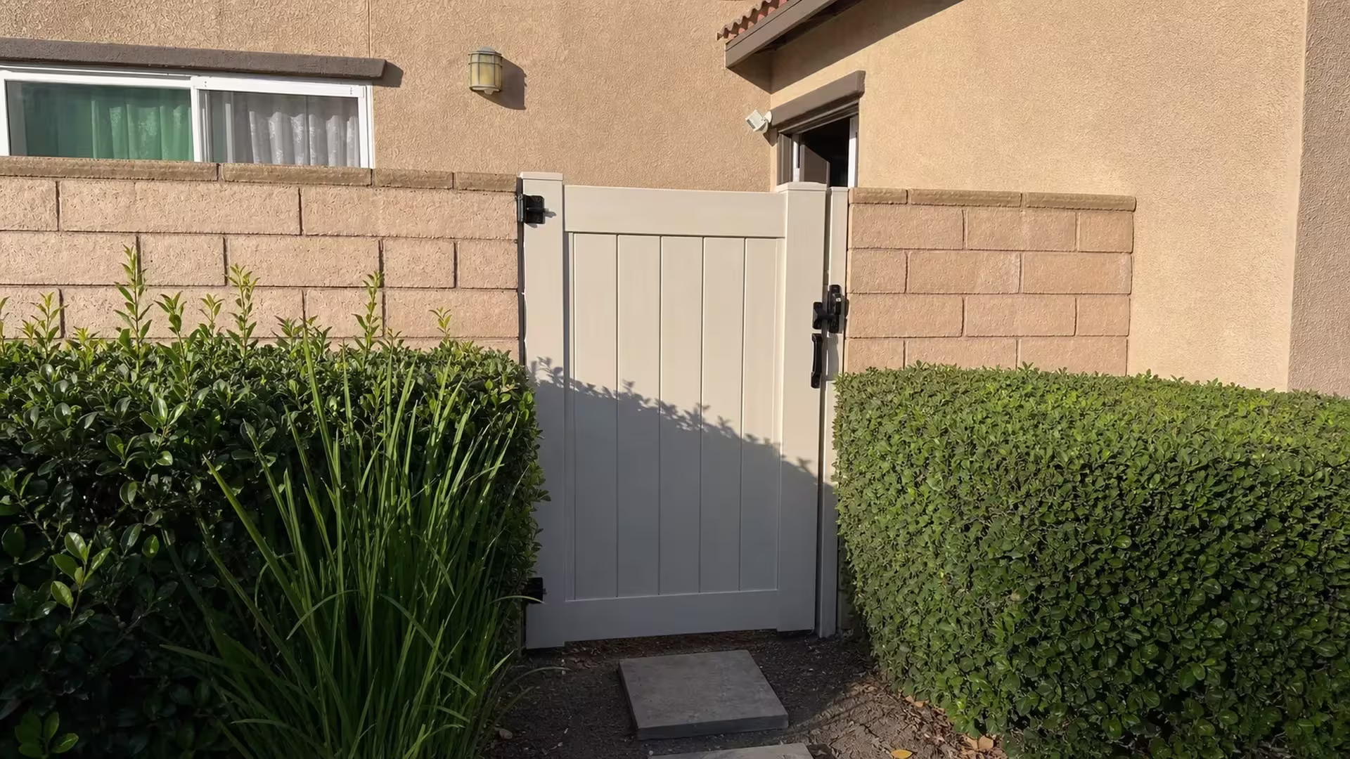 A wall lantern and curtained window sit above this closed White vinyl gate, set between tan block walls in Ontario