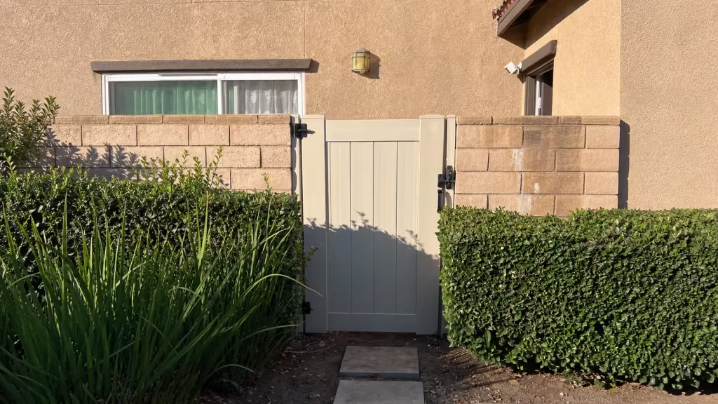 Stepping stones and a soil planting bed lead to the new White vinyl privacy gate between matching tan block walls in Ontario