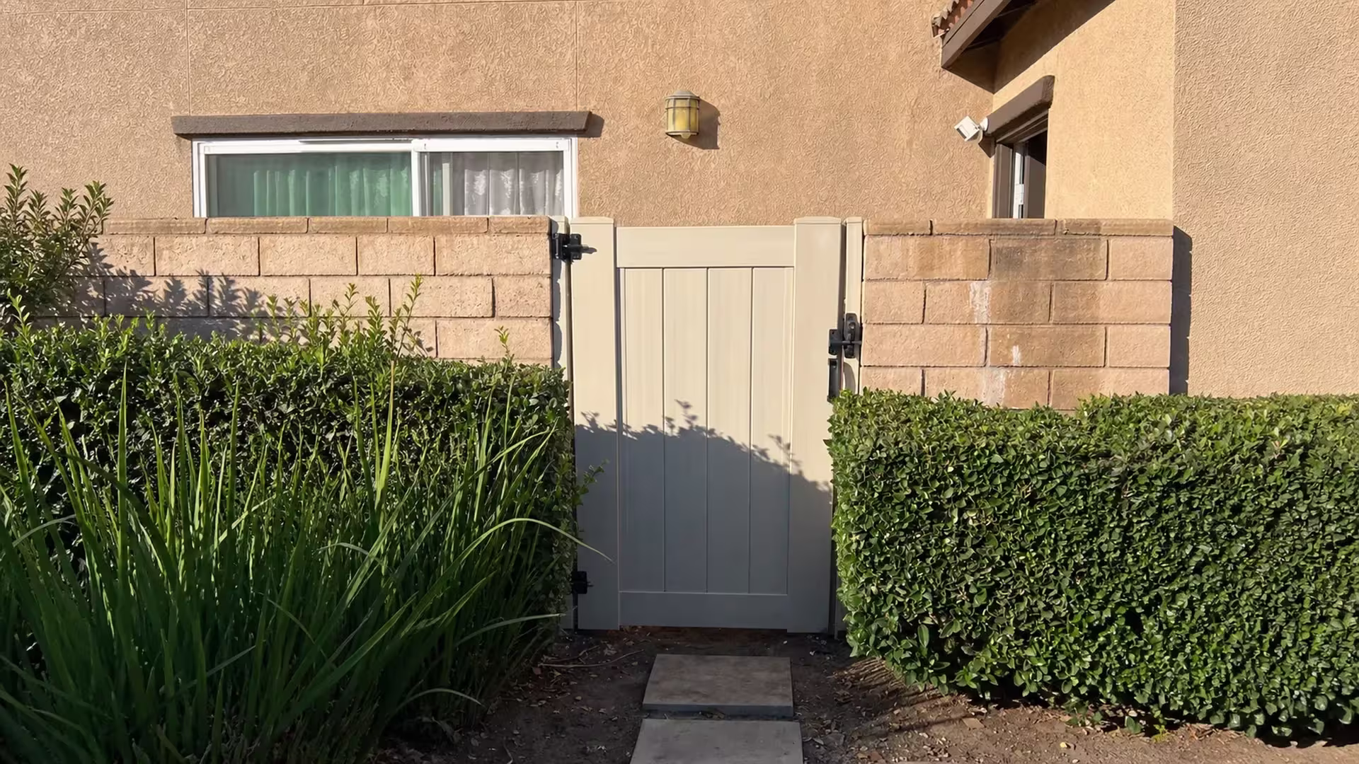 Stepping stones and a soil planting bed lead to the new White vinyl privacy gate between matching tan block walls in Ontario