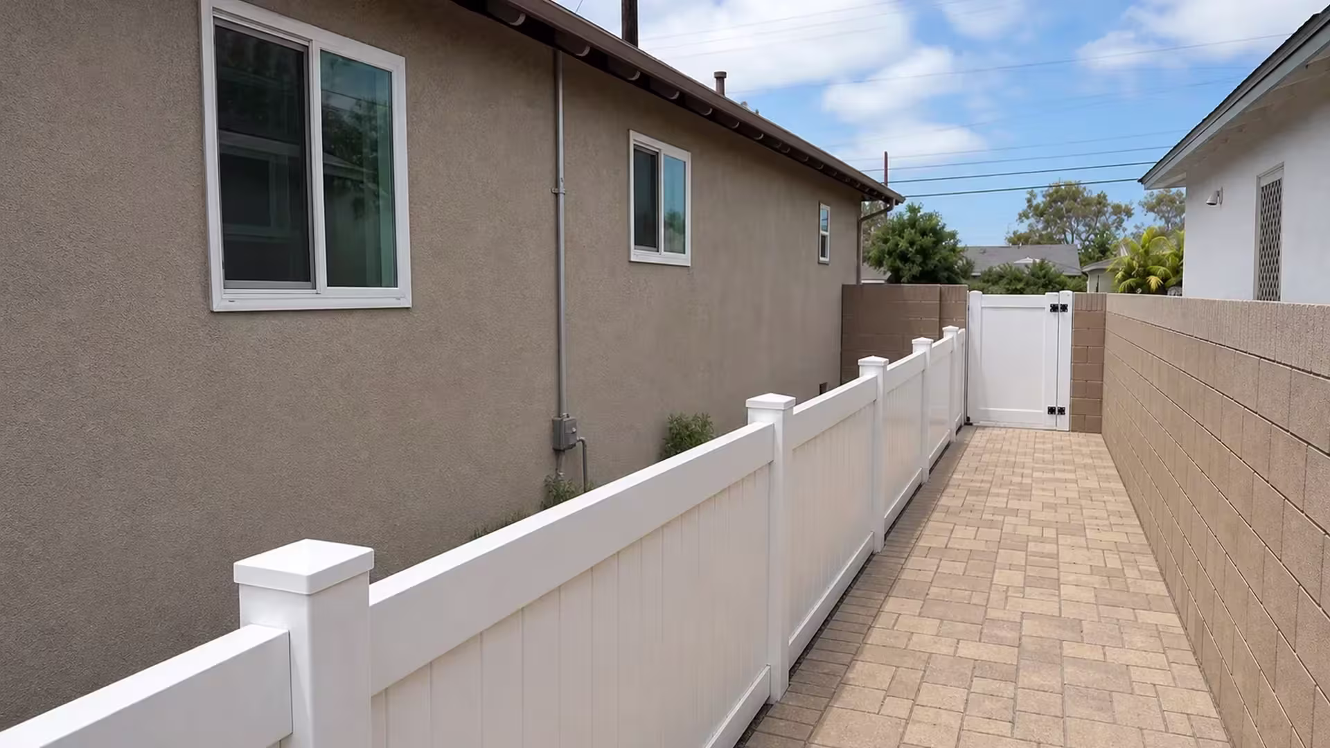 A narrow grass strip opposite the paver walkway runs beside this White vinyl fence and gate in Torrance