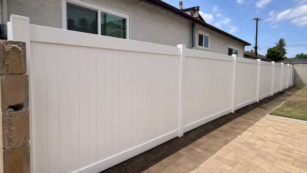 A tan masonry column marks the paver walkway beside this White vinyl privacy fence in Torrance