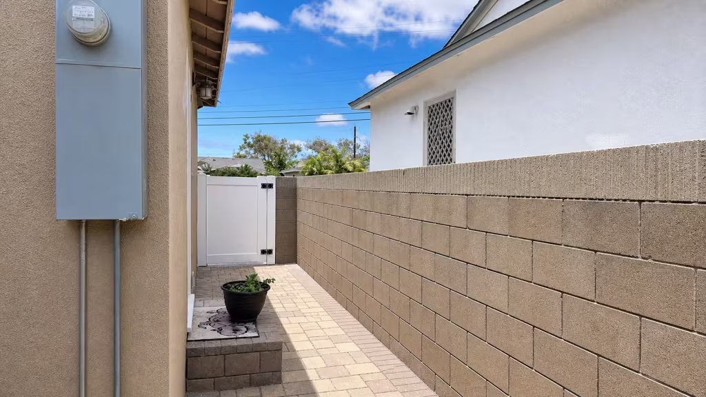 A raised block planter sits beside this White vinyl gate on the privacy fence, spanning a tan paver walkway in Torrance